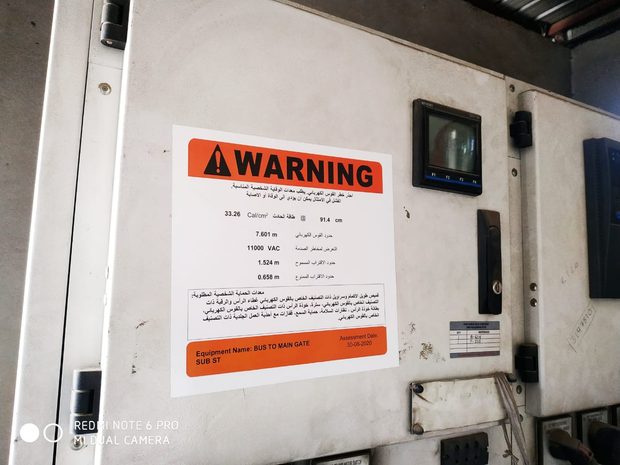 Bilingual Arabic and English arc flash warning label installed on switchgear, showing a high incident energy value and a larger arc flash boundary