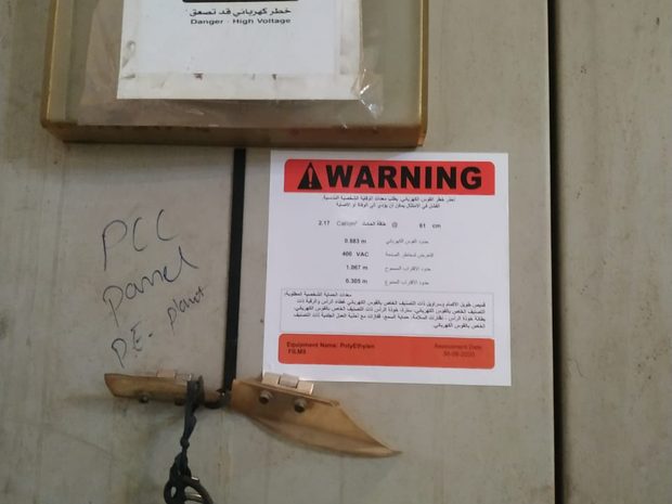 Bilingual Arabic and English arc flash warning label installed on a panel, showing a low incident energy value at the working distance