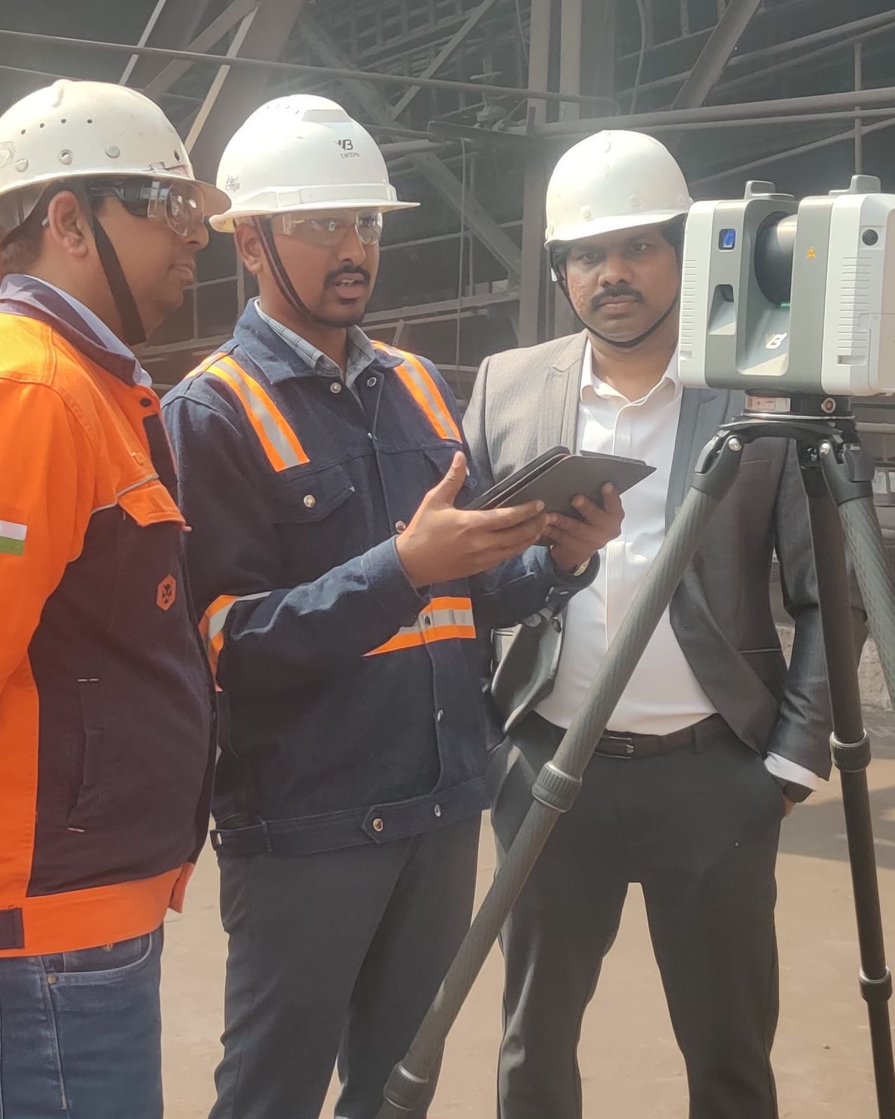 VB engineers in hard hats reviewing captured field data on a tablet beside a laser scanner