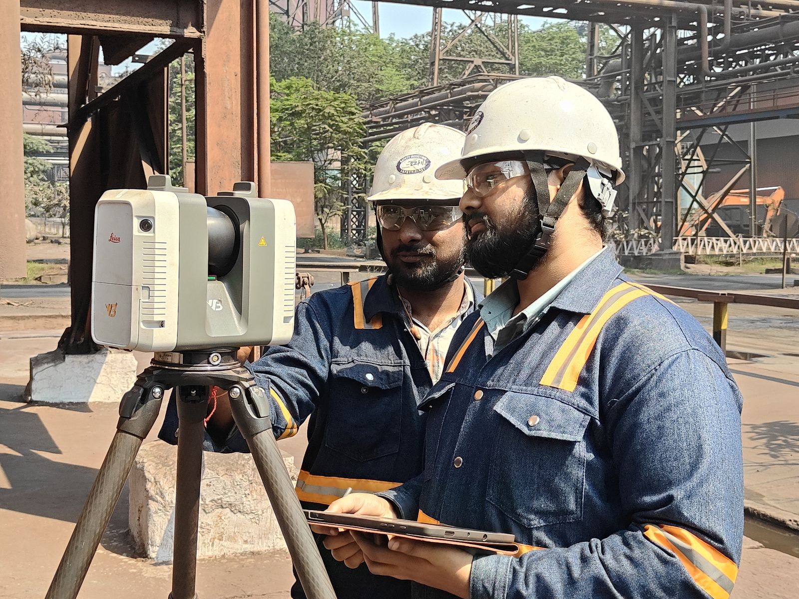 Two VB engineers in hard hats operating a Leica laser scanner and tablet at a steel plant