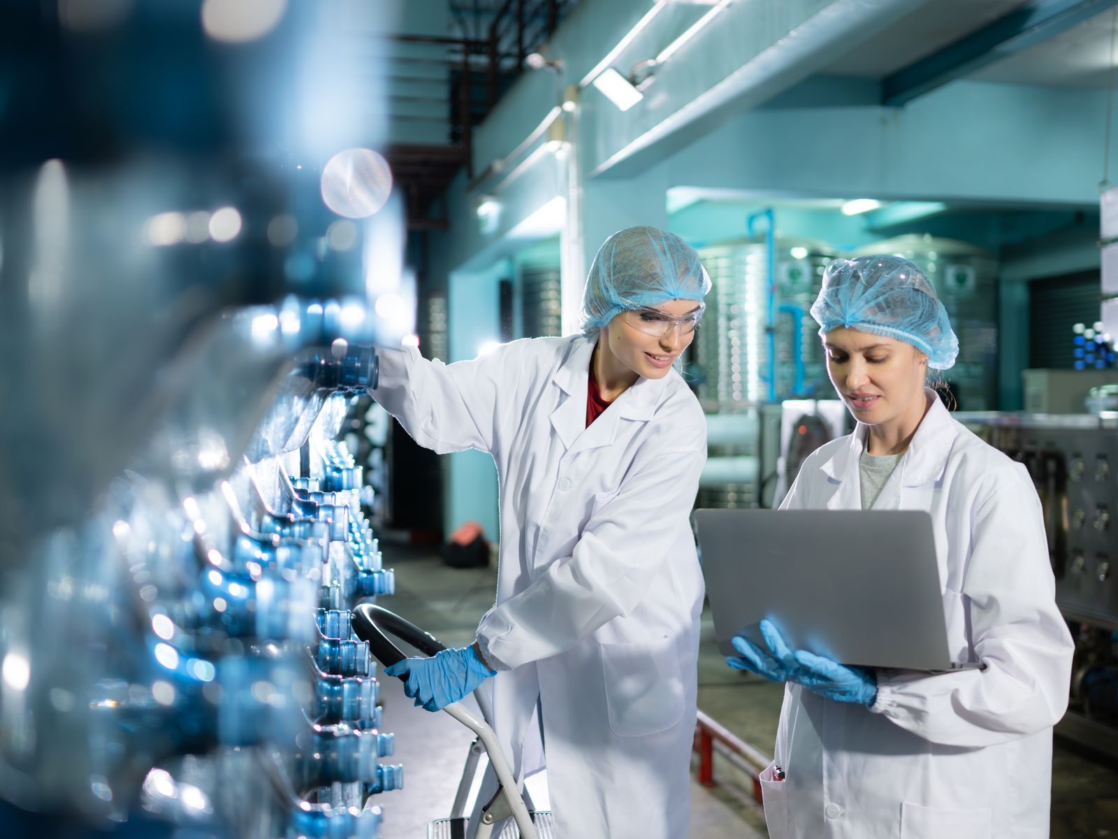 Two production workers in hairnets, lab coats and gloves checking a filling line