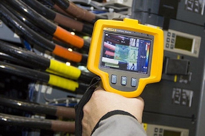 Hand-held thermal imager pointed at cable terminations and breakers inside an open panel