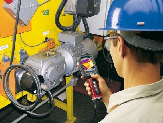 Technician in a hard hat scanning a running motor and its terminal box with a thermal imager