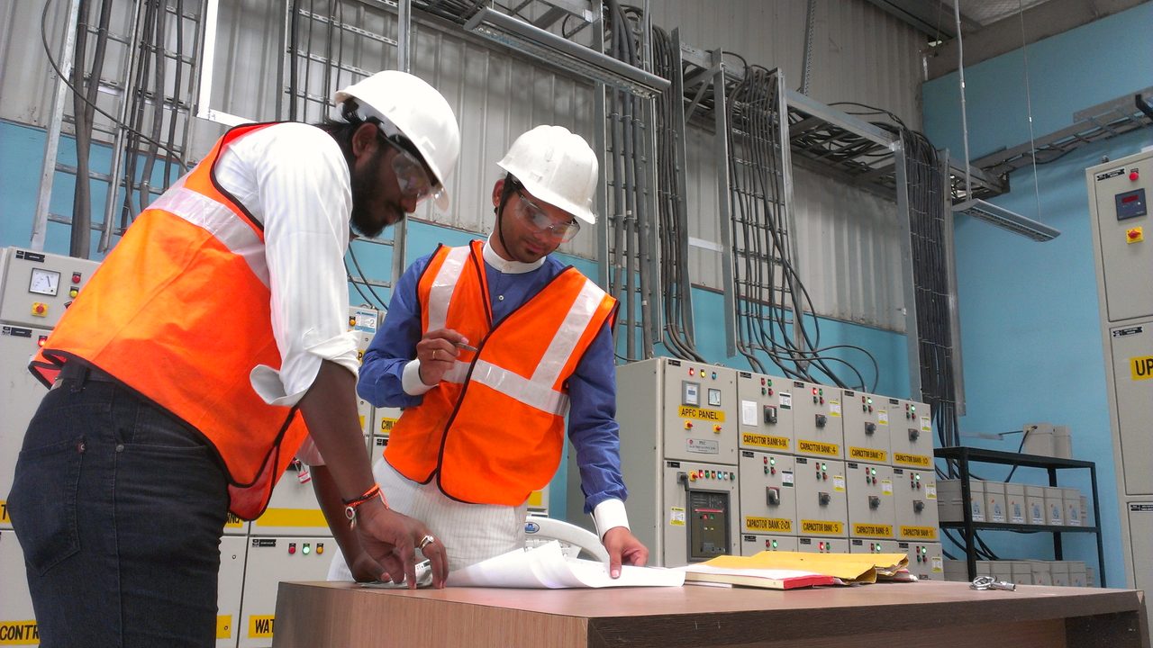 Two VB engineers reviewing a one-line diagram at a table in front of a low-voltage switchgear and MCC lineup